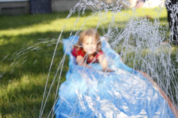 Smiling girl sliding down an outdoor slip and slide. selective focus on water in front of child stock photo