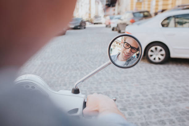 istock Guy is looking in small mirror he has on motorcycle. Guy is sitting on this vehicle. He is standing in middle of road 993653420