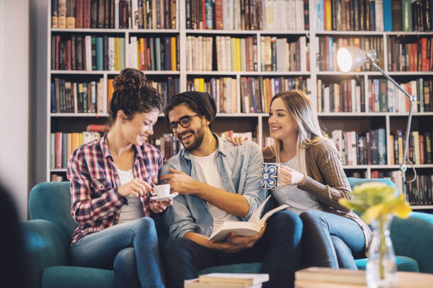 istock Group of cute joyful students heaving meeting for a break while sitting on the sofa in the library. 993658022