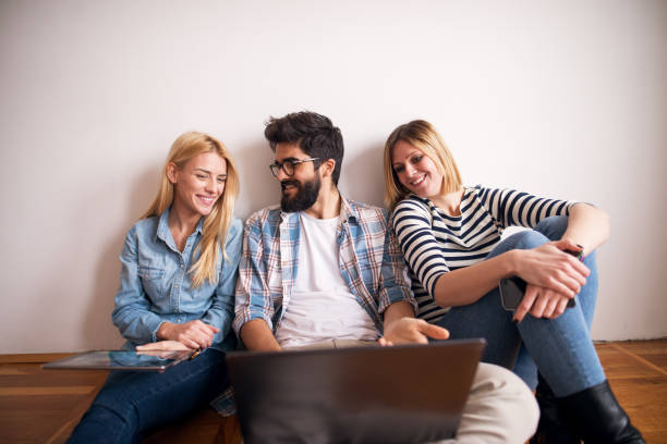 istock Group of cheerful people is sitting on a floor leaning against the wall while talking and using laptop. 993662998