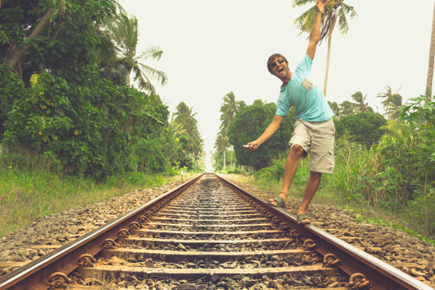 Young man walking on railroad track while listening to music with headphones on his smartphone in rural area in Bentota, Sri Lanka. Vintage effect