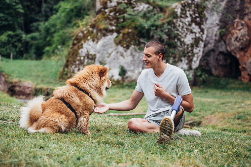 One man, disability young man with prosthetic leg his dog best friend relaxing together in nature.