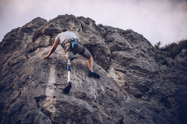 Disability man climbing rocks One man, disability young man with prosthetic leg free climbing on a rock in nature.. disabled person hiking outdoors stock pictures, royalty-free photos & images