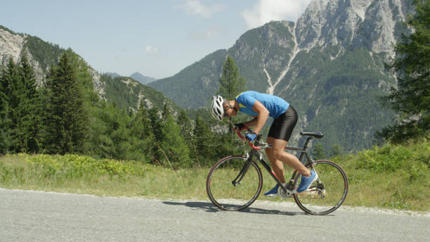 Pro road cyclist enduring a difficult mountain ascent on his cool bicycle. Pro road cyclist enduring a difficult mountain ascent on his cool bicycle. Determined Caucasian sportsman looks down and grits his teeth as he ascends a challenging mountain in the hot summer sun. steep photos stock pictures, royalty-free photos & images