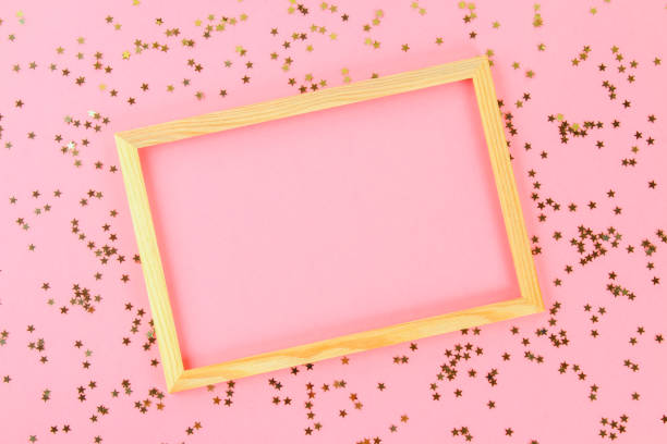 istock A wooden empty frame on a pastel background surrounded by shiny decorative stars and balls. 993728748