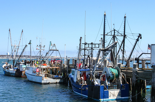 Fishing boats moored at the dock with a pick-up truck with the door open and the opposite shore visable across the bay