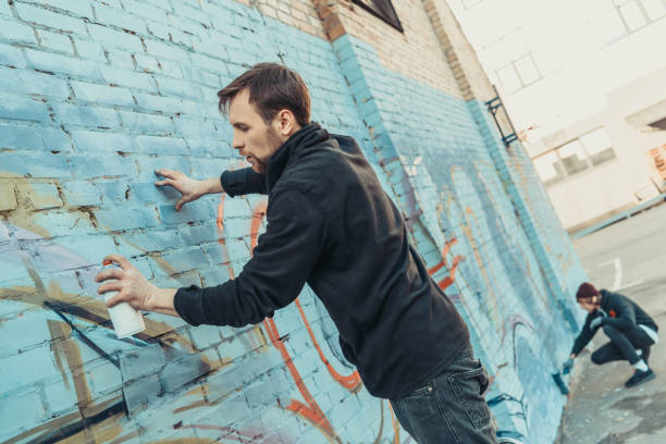 street artists painting colorful graffiti on wall of building - graffiti men wall street art imagens e fotografias de stock