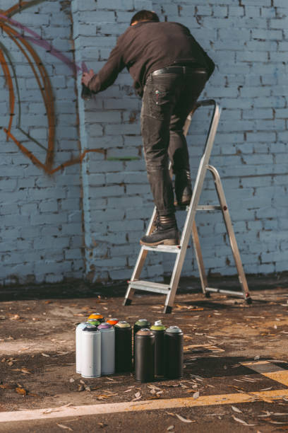 istock man standing on ladder and painting colorful graffiti on building 993740732