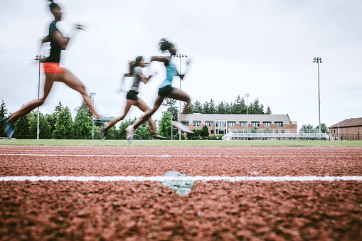 Young adult women sprint down the track, their motion intentionally blurred to show their speed.  Training for track and field competition.