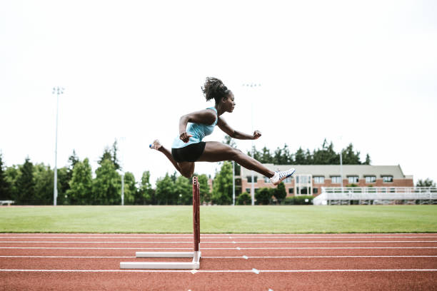 спортсменка-женщина работает hurdles для легкой атлетики - hurdle hurdling track event women стоковые фото и изображения