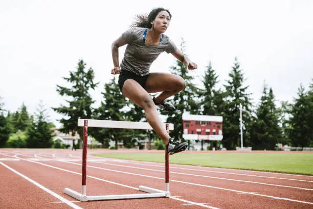 A young woman does hurdling training for her track competition training.  Captured mid- jump. Horizontal image.