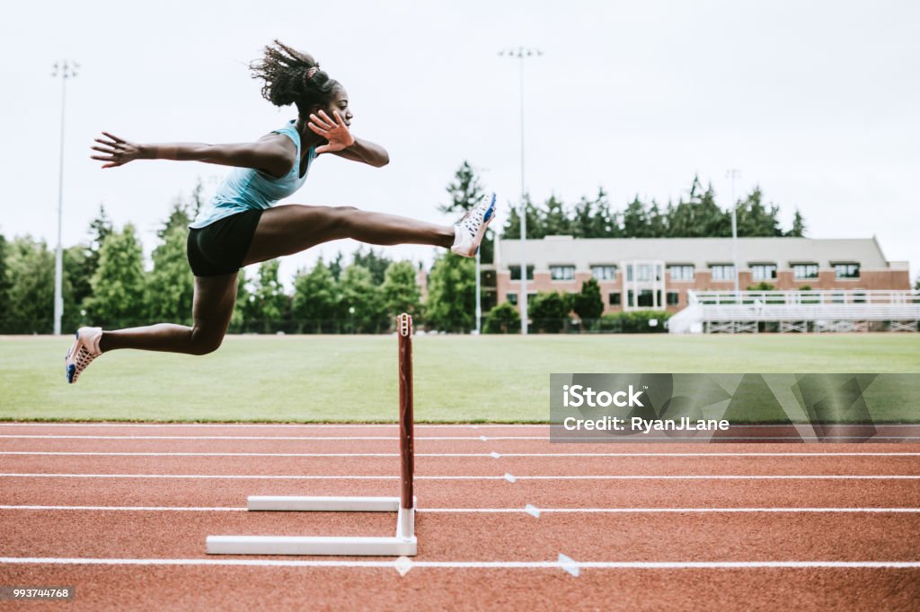 Woman Athlete Runs Hurdles for Track and Field A young woman does hurdling training for her track competition training.  Captured mid- jump. Horizontal image with copy space. Athlete Stock Photo