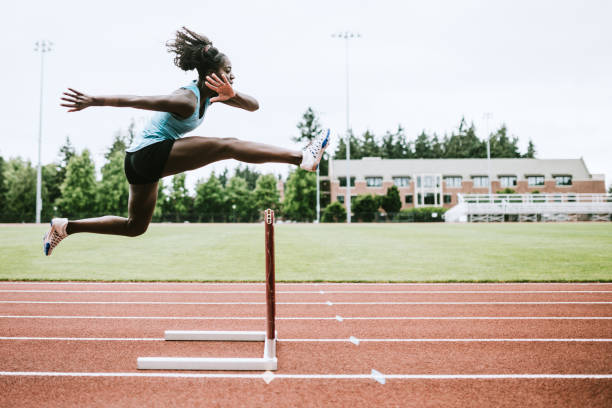 Woman Athlete Runs Hurdles for Track and Field A young woman does hurdling training for her track competition training.  Captured mid- jump. Horizontal image with copy space. athletes stock pictures, royalty-free photos & images