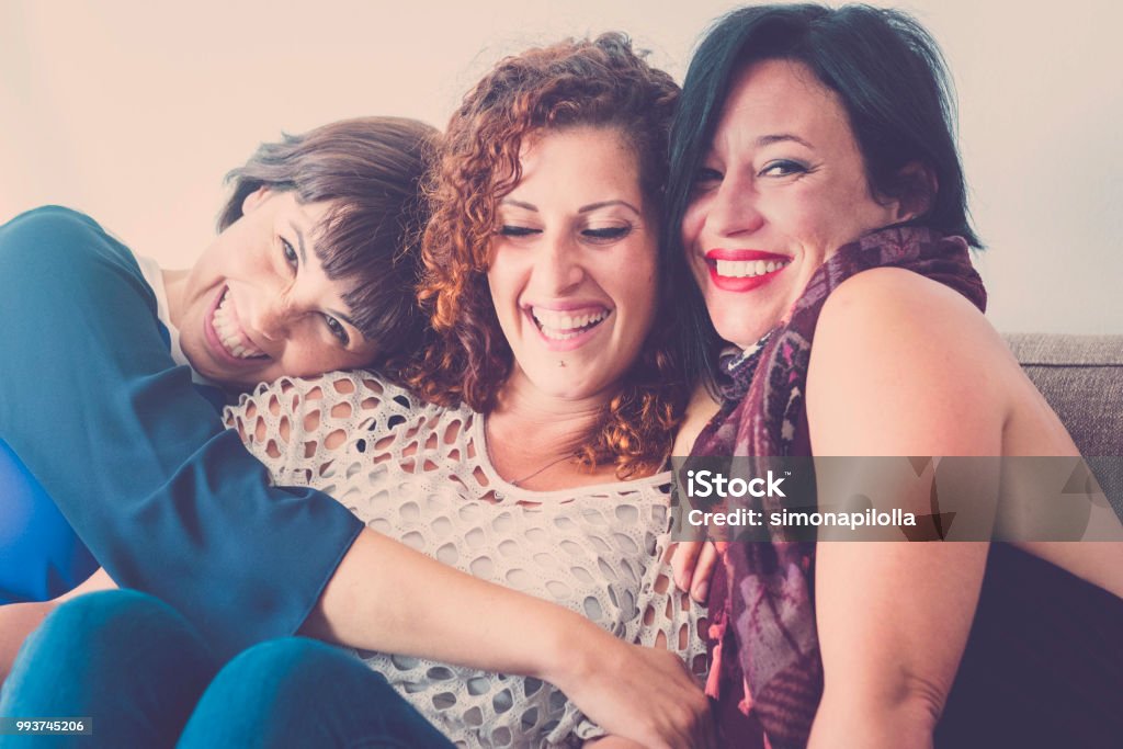 cheerful females middle age young womens friends together sitting on a sofa at home in leisure activity indoor. smile and enjoy the day hugging and touching with care and friendship Friendship Stock Photo