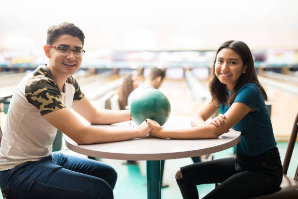 テーブルの上で手を繋いでいるボウリングのボールで十代のカップル - bowling holding bowling ball hobbies ストックフォトと画像