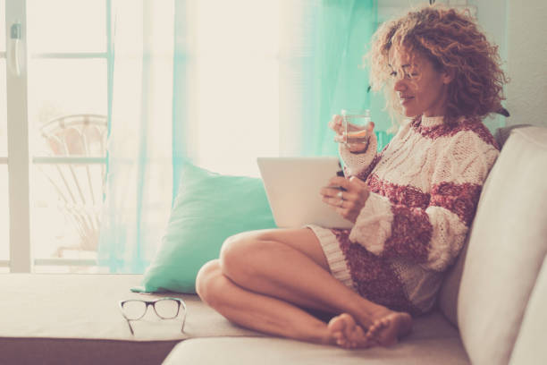 istock middle age beautiful model woman sitting at home on the sofa reading an e-book on tablet connected with internet. office work indoor alternative lifestyle with independent day and enjoying life 993749246