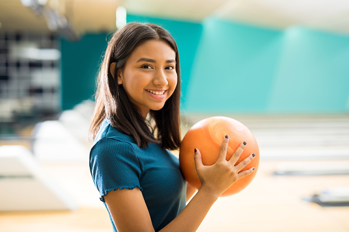 Smiling teenage girl with ball having fun at bowling alley in club