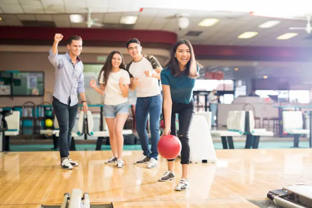 Photo of Friends Motivating Teen Girl Throwing Bowling Ball At Alley