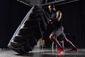 side view of athletic african american man exercising with tyre and looking away in gym