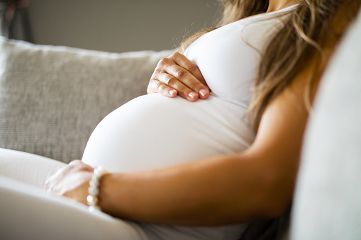 Primer plano de mujer embarazada sentada en el sofá con las manos en el vientre photo