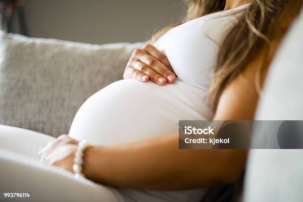 Closeup Of Pregnant Woman Sitting In Sofa With Her Hands At Belly Stock Photo - Download Image Now