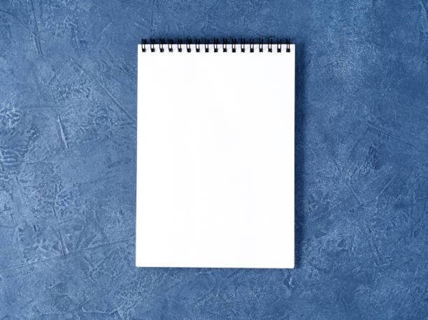 istock The open notepad with clean white page on aged dark blue stone table, top view 993954110