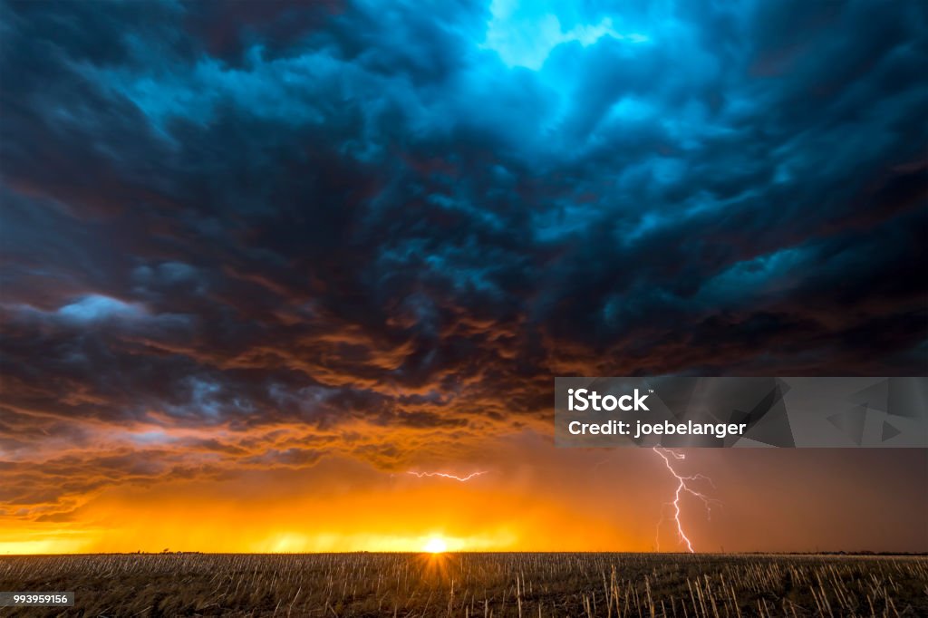 Large lightning strike at dusk on Tornado Alley A nighttime, tornadic mezocyclone lightning storm shoots bolt of electricity to the ground and lights up the field and dirt road in Tornado Alley.

A large lightning strike at dusk in an open plain framed against a deep, dark orange sunset and stormy skies. 

A large lightning strike at dusk in an open plain framed against a deep, dark orange sunset and stormy skies. Sky Stock Photo