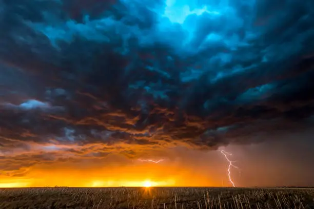 A nighttime, tornadic mezocyclone lightning storm shoots bolt of electricity to the ground and lights up the field and dirt road in Tornado Alley.

A large lightning strike at dusk in an open plain framed against a deep, dark orange sunset and stormy skies. 

A large lightning strike at dusk in an open plain framed against a deep, dark orange sunset and stormy skies.