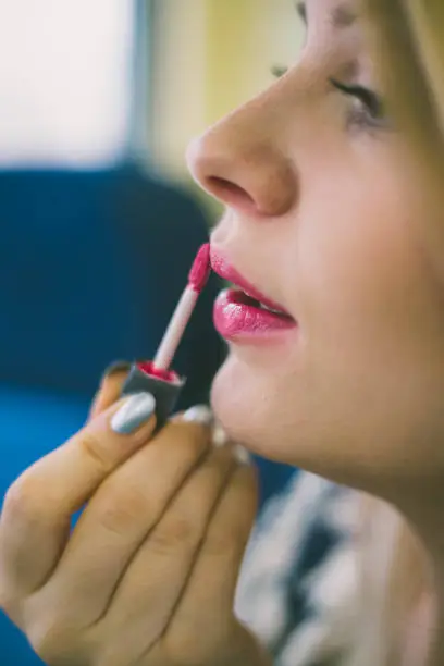 Photo of Closeup portrait of cute young girl putting red lipstick on