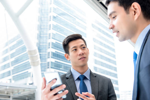 istock Businessmen discussing information on smartphone outdoors 993970084