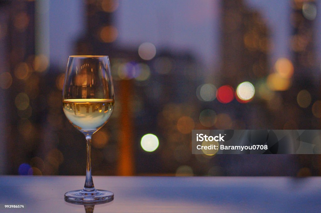 A glass of white wine on table of rooftop bar with colorful bokeh. A glass of white wine on table of rooftop bar with colorful bokeh of city light and space for text. Rooftop Stock Photo