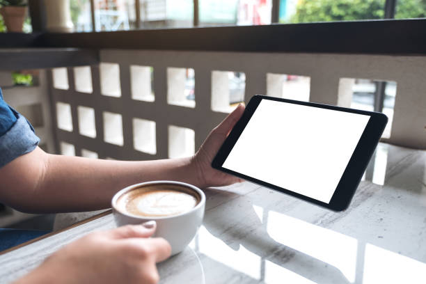istock Mockup image of a woman holding black tablet pc with white blank screen while drinking coffee in cafe 994020522