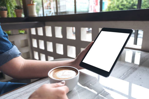 istock Mockup image of a woman holding black tablet pc with white blank screen while drinking coffee in cafe 994020524