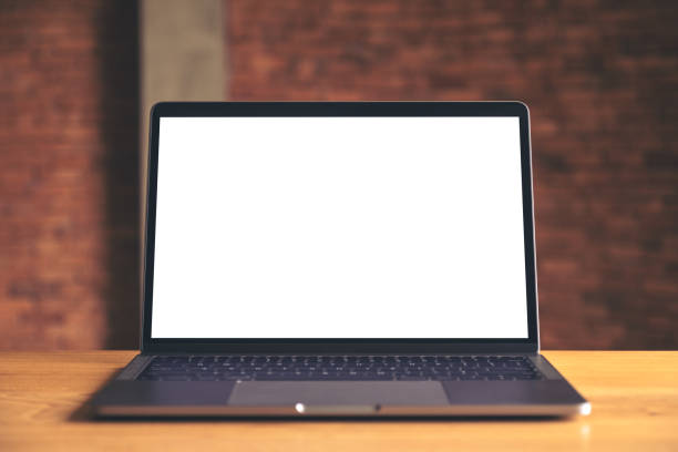 istock Mockup image of laptop with blank white desktop screen on wooden table with concrete wall background 994020696