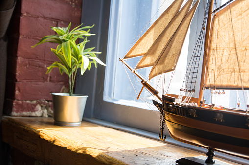 Model of a boat and flower in a pot on a wooden window sill in an old house.