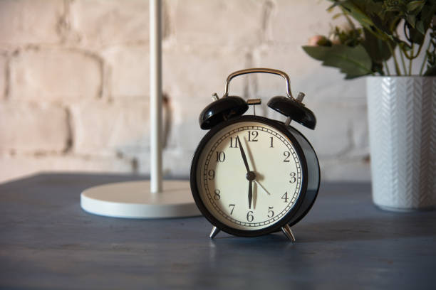 istock Alarm clock with table lamp and flower in pot on nightstand 994077402