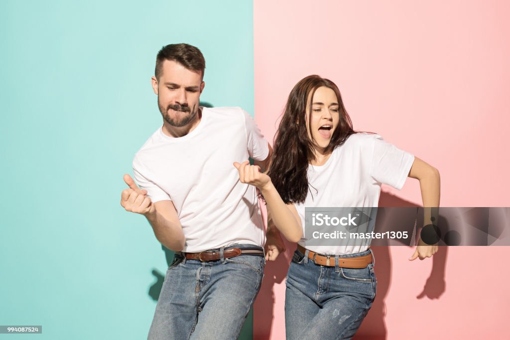 A couple of young man and woman dancing hip-hop at studio A couple of young funny and happy man and woman dancing hip-hop at studio on blue and pink trendy color background. Human emotions, youth, love and lifestyle concept Dancing Stock Photo