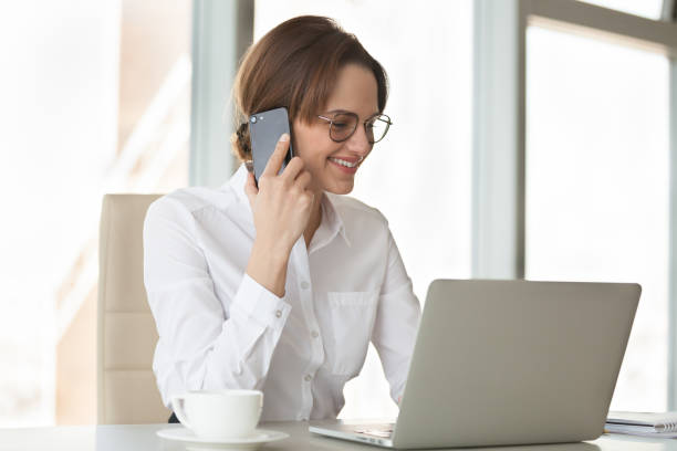 istock Smiling confident businesswoman making phone call using laptop in office 994101672