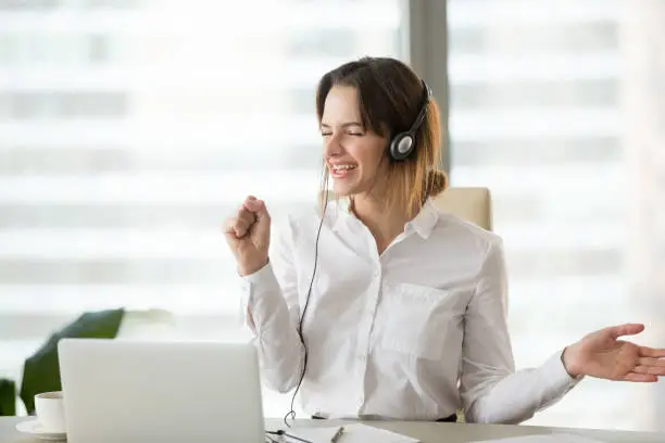 Photo of Excited happy businesswoman listening to music in headphones at work
