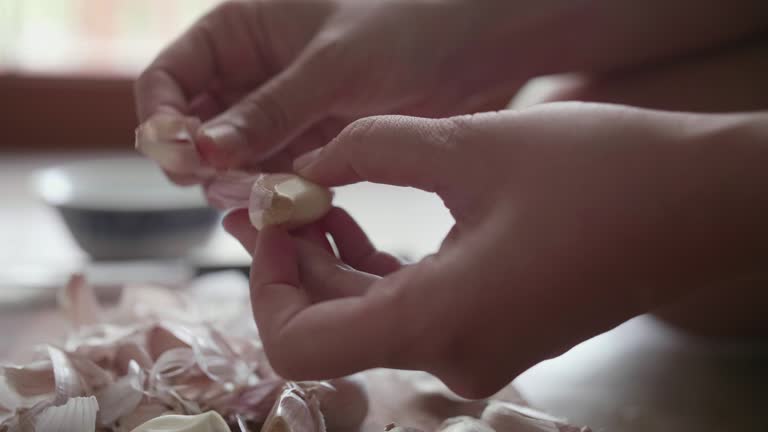 Hand peeling garlic on wooden chopping board