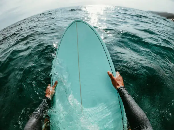 First person point of view photo of a surfer floating in the ocean while catching the waves on his surfboard