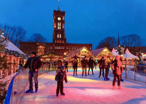 Berlin, Germany - December 10, 2017: People on Ice skating Rink at Night Christmas Market on Town Hall in Winter Berlin, Germany. Advent Fair Decoration and Stalls with Crafts Items on the Bazaar.