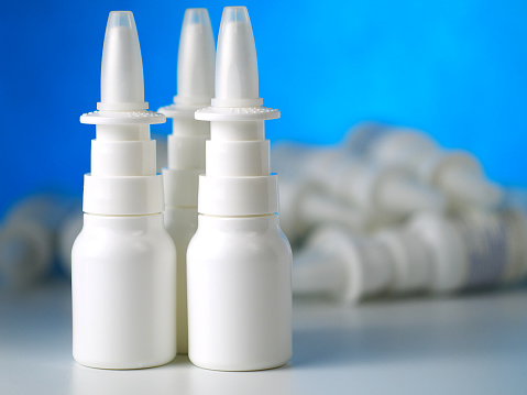 three nasal spray bottles in front of other bottles heap, shallow depth of field