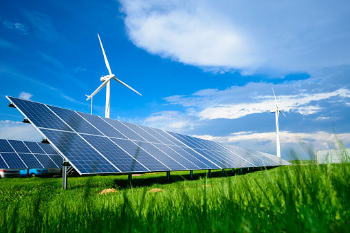 Solar energy panels and windmills against blue sky on summer day, background