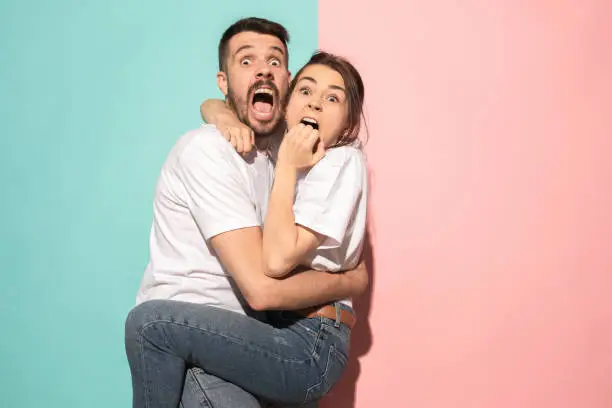 We are in awe. Fright. Portrait of the scared man and woman. Couple standing on trendy pink and blue studio background. Human emotions, facial expression concept. Front view