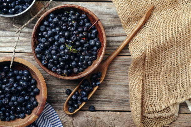 istock Three bowls with forest blueberry just picked and kept unwashed. Wooden rustic background, linen and striped towel. Harvest. Top view with copy space 994163294