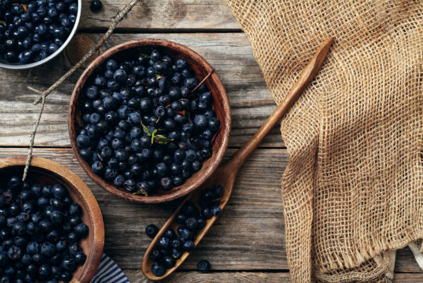 istock Three bowls with forest blueberry just picked and kept unwashed. Wooden rustic background, linen and striped towel. Harvest. Top view with copy space 994163346