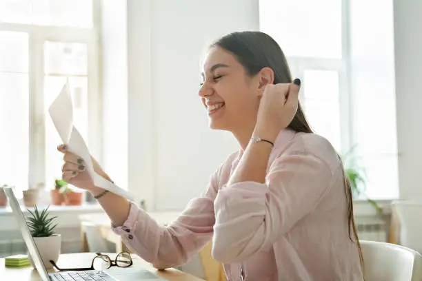 Photo of Happy female employee excited reading promotion letter