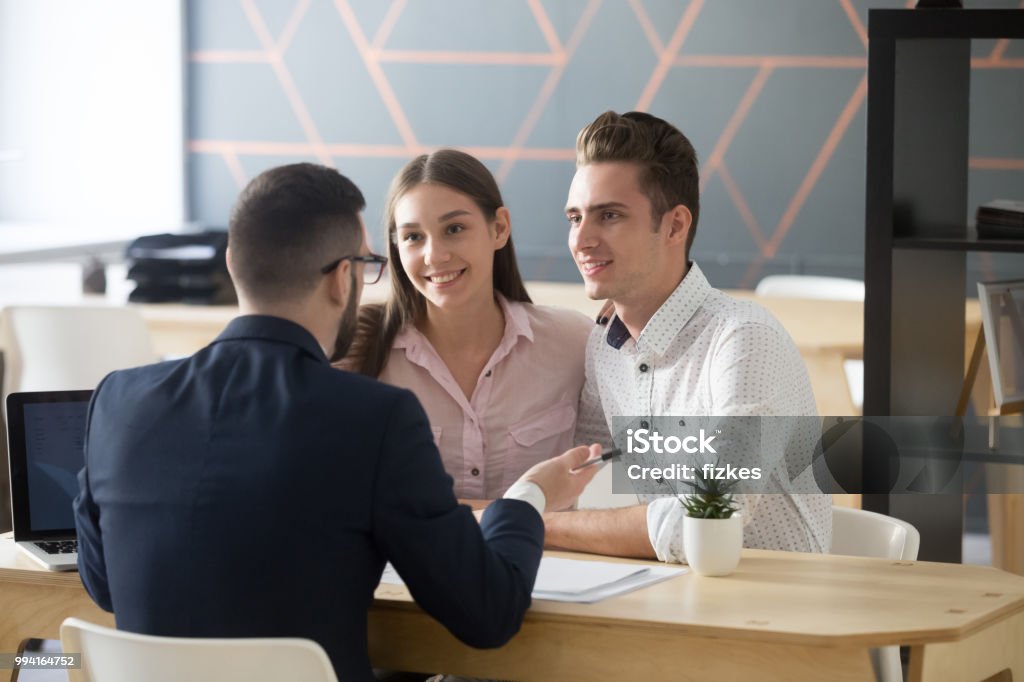 Insurance agent consulting millennial couple in office Insurance agent or broker consulting smiling millennial couple on property purchase, Real Estate Agent discussing mortgage loan with young spouses, explaining contract terms at meeting or negotiations in office Financial Advisor Stock Photo