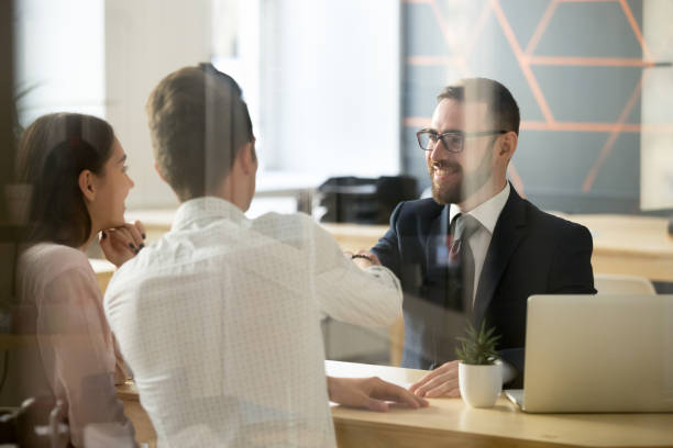 mannelijke makelaar handshaking klanten na succesvolle onderhandelingen in kantoor - bank stockfoto's en -beelden